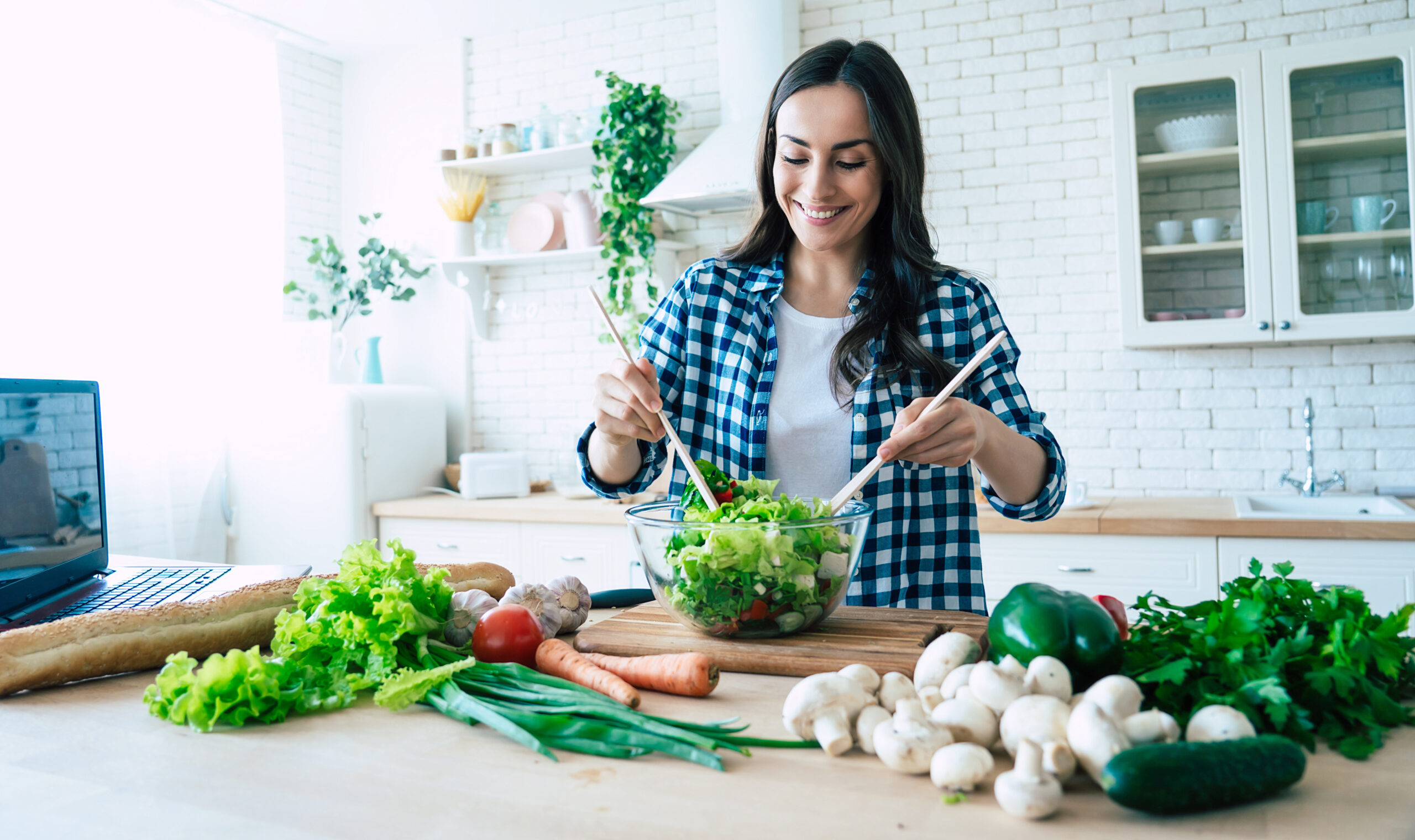 Beautiful young woman is preparing vegetable salad in the kitche